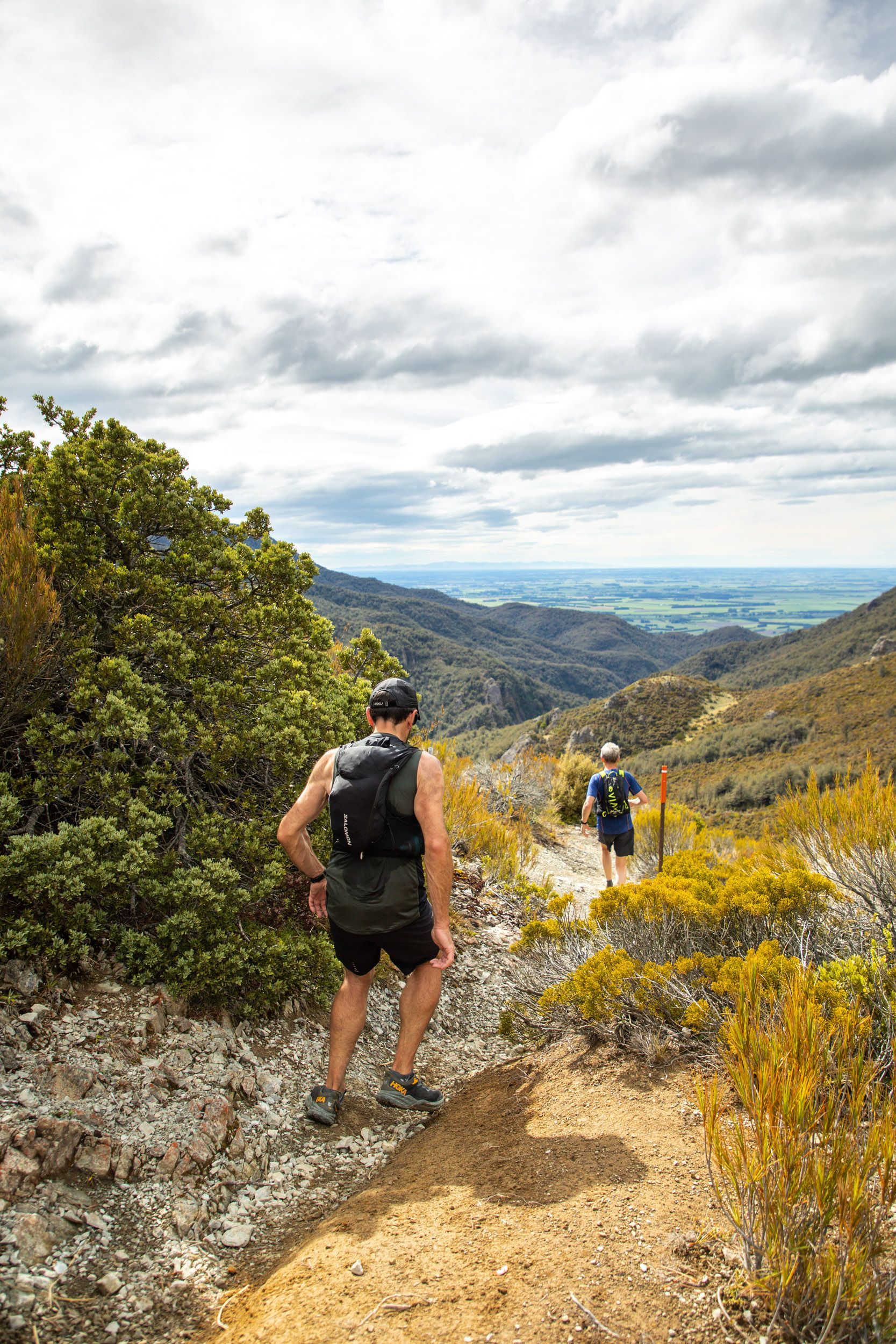Two people are hiking down a dirt path in the mountains.