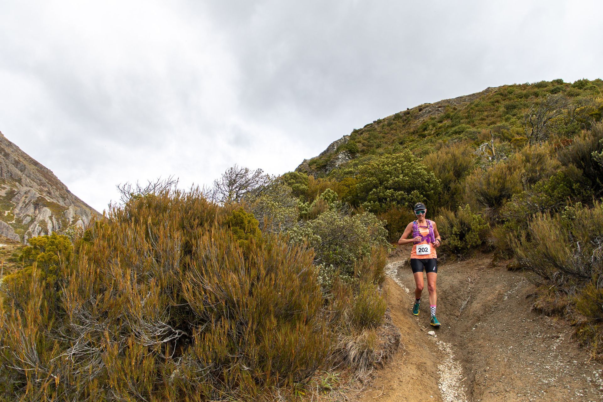A woman is running down a dirt path in the mountains.