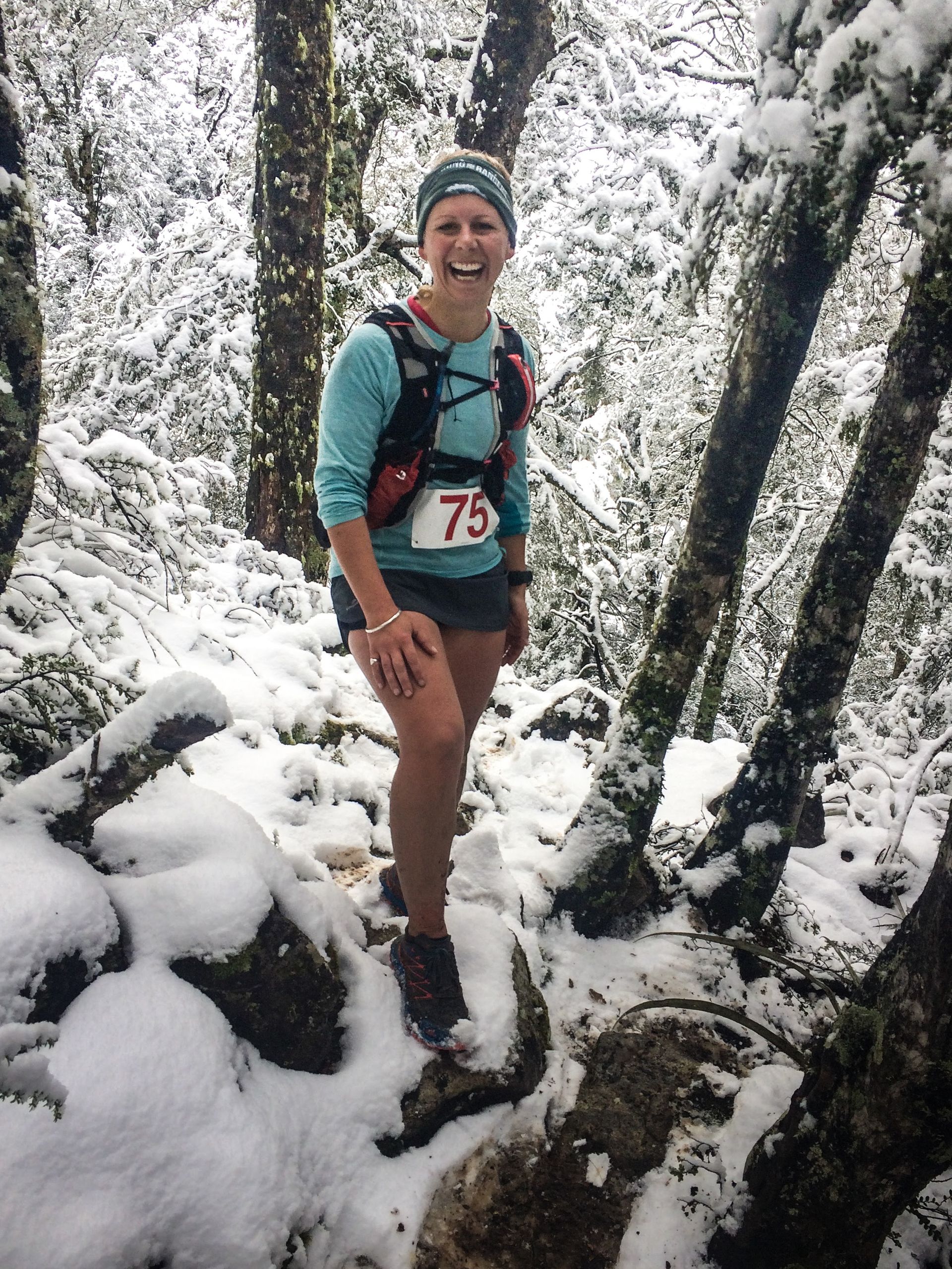 A woman is standing in the snow in the woods.