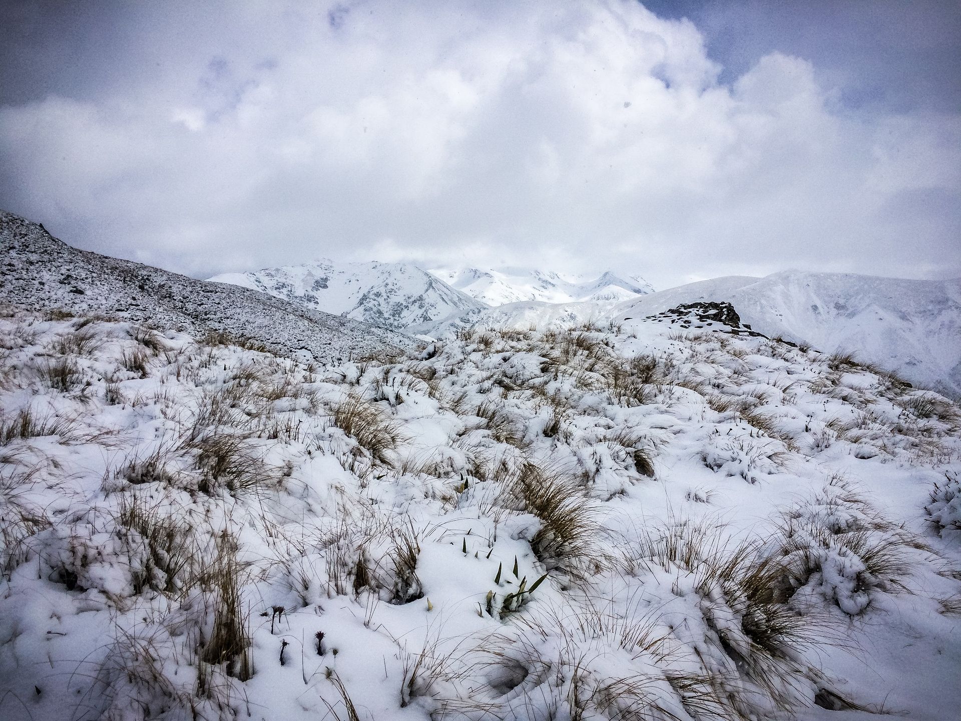 A snowy field with mountains in the background and a cloudy sky