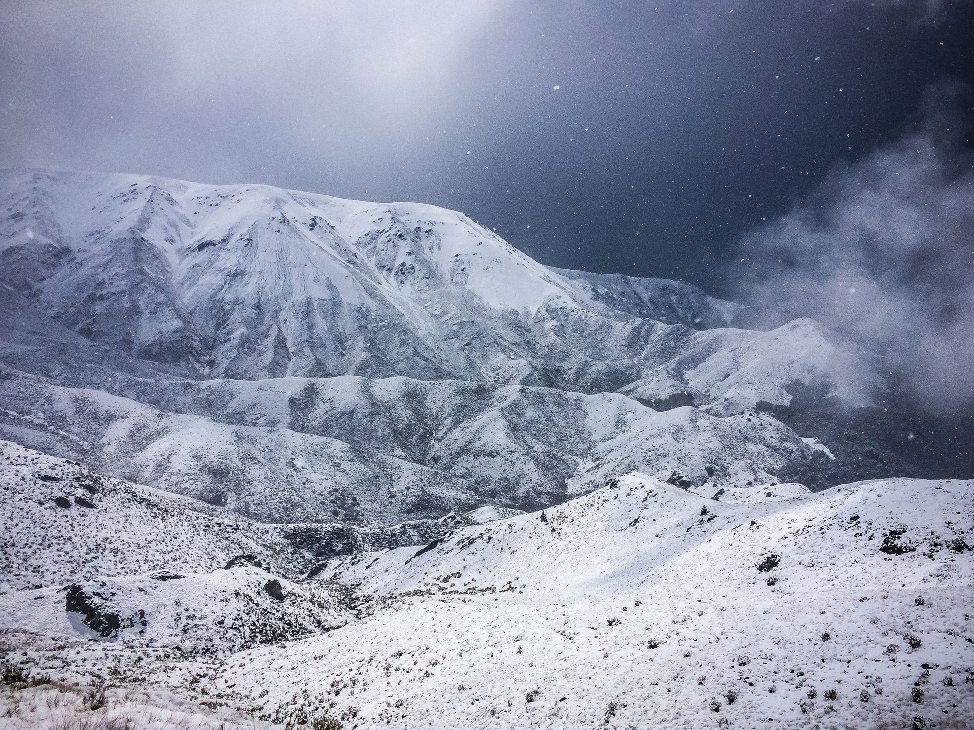 A snowy mountain covered in snow with a dark sky in the background.