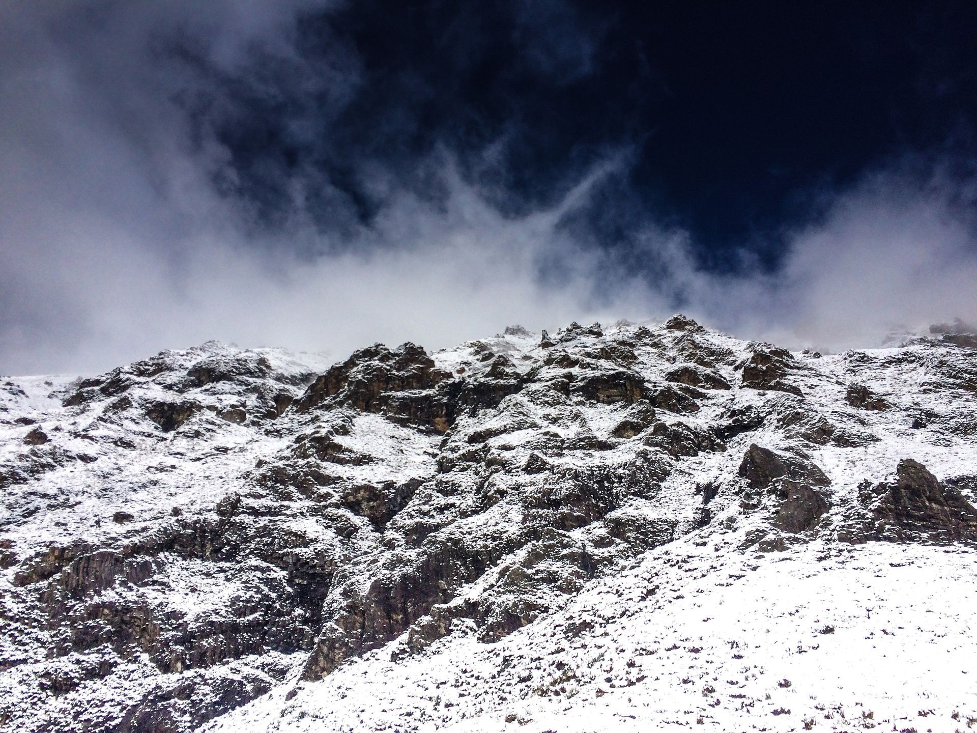 A mountain covered in snow and rocks with a cloudy sky in the background