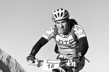 A man wearing a helmet is riding a bike with the number 16 on the handlebars