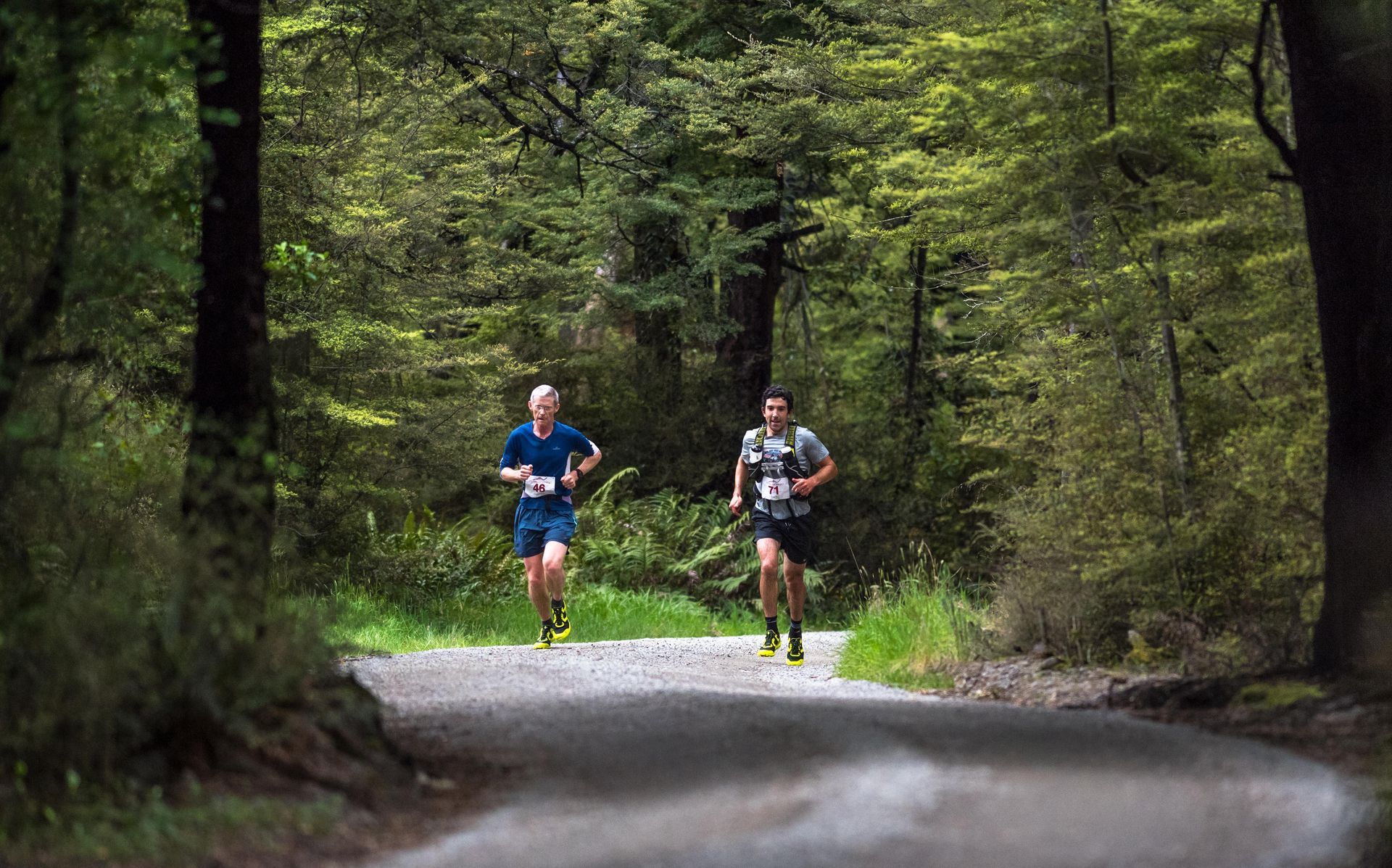 Two men are running down a dirt road in the woods.
