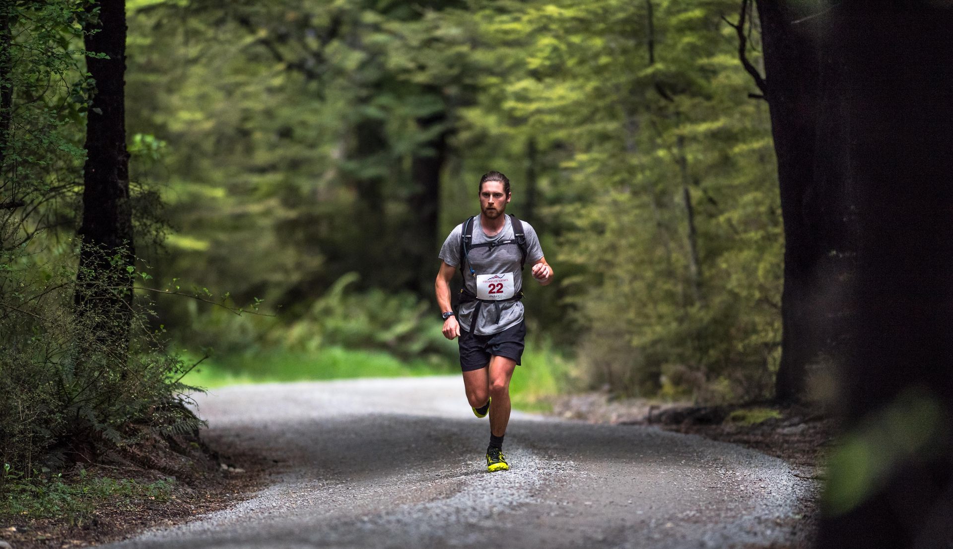 A man is running down a dirt road in the woods.