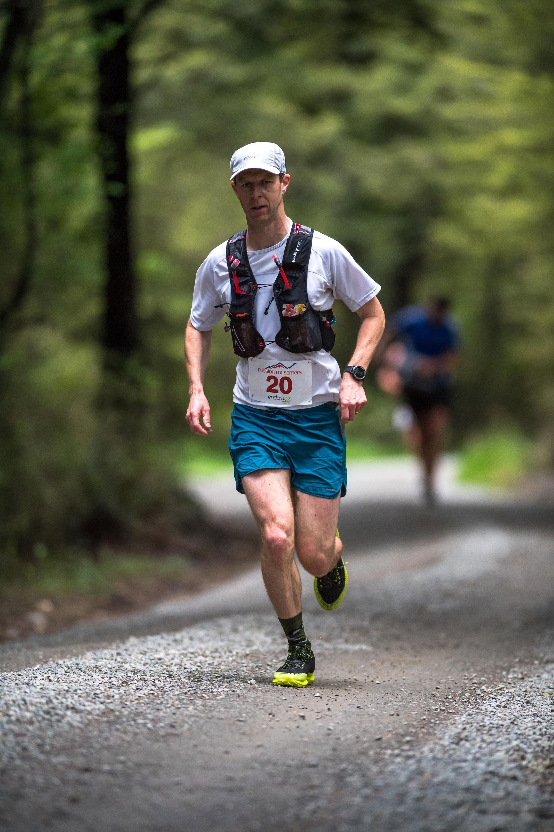 A man is running down a dirt road in the woods.
