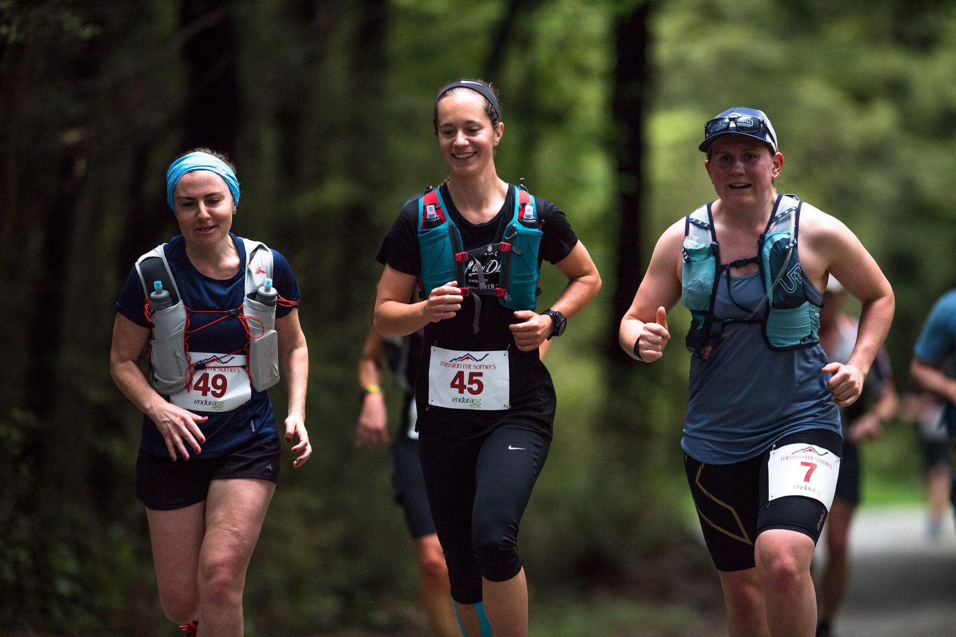 A group of women are running a trail race in the woods.