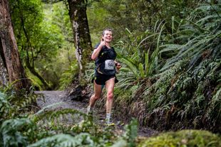 A woman is running on a trail in the woods.