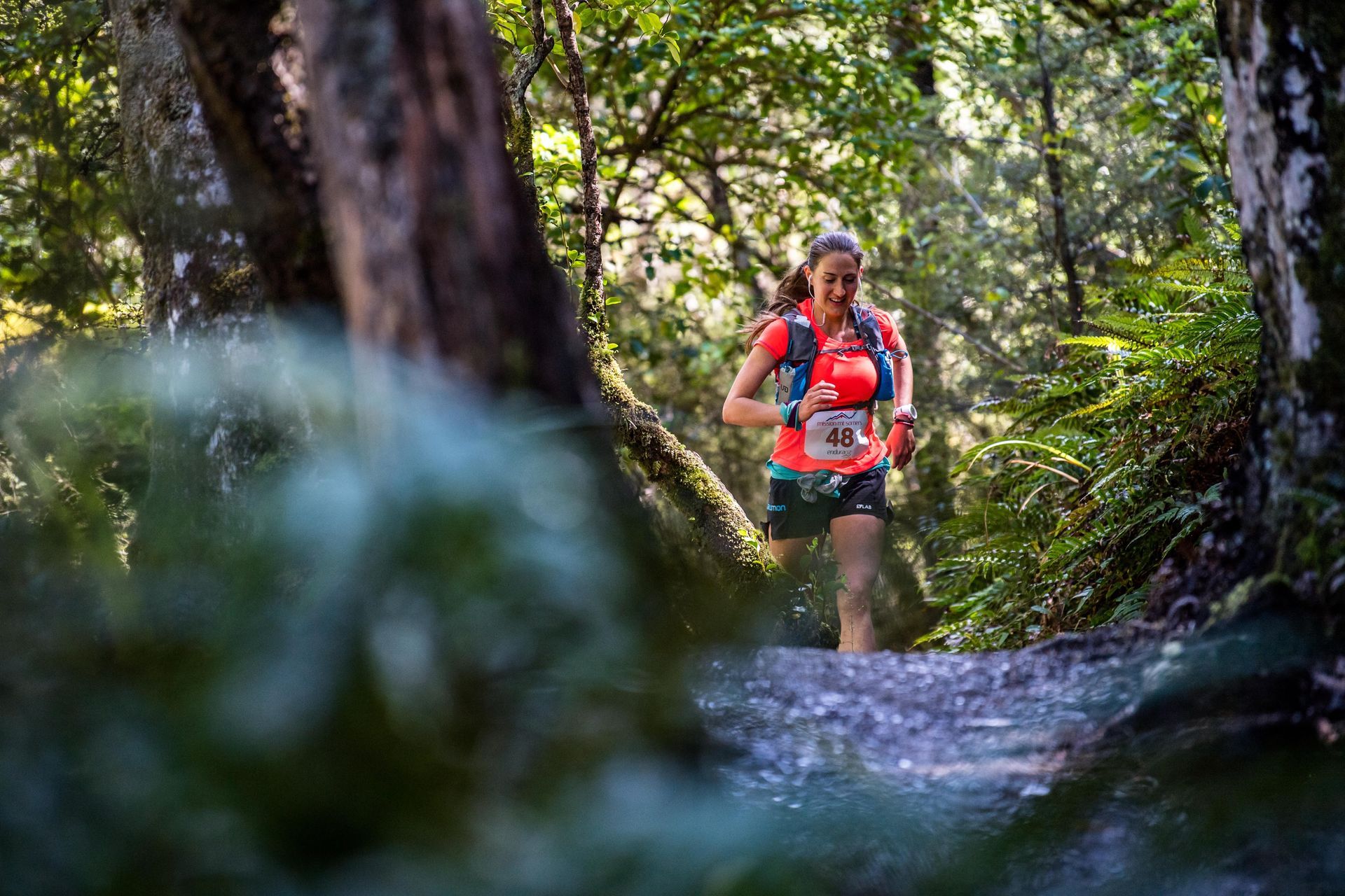 A woman is running through a stream in the woods.