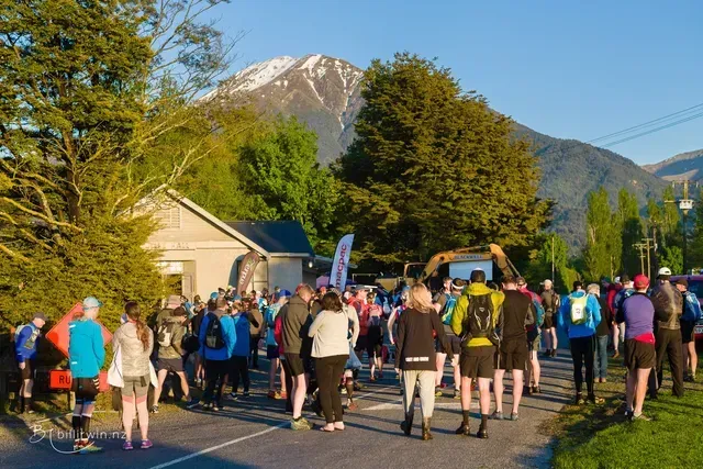A group of people are standing on the side of a road in front of a mountain.