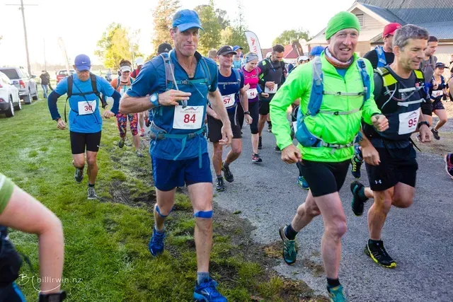 A group of people are running a race and one of them has the number 84 on his shirt.