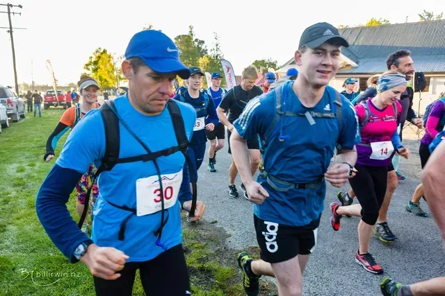 A group of people are running a race and one of them has the number 30 on his shirt.