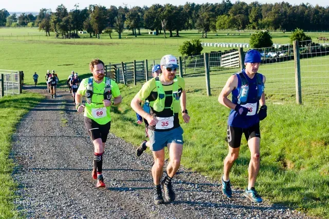 Three men are running down a dirt road in a field.