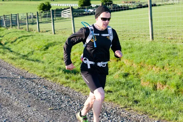 A man with a backpack is running down a gravel road.