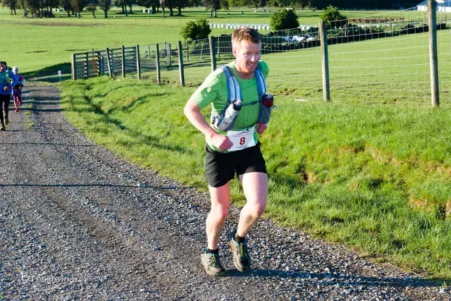 A man in a green shirt is running down a dirt road.