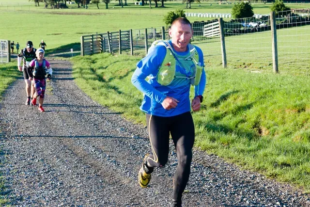 A man in a blue shirt is running down a dirt road.