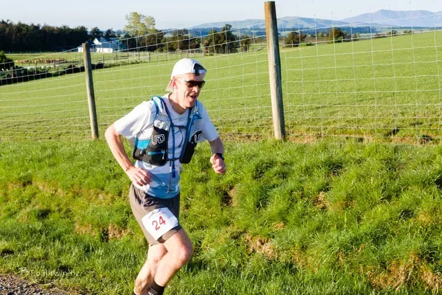 A man is running in a field with a fence in the background.