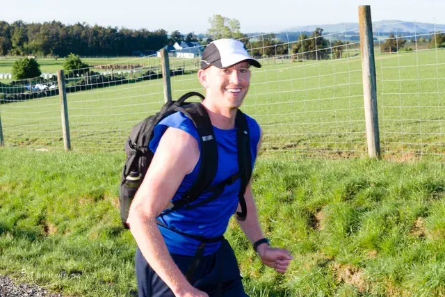 A man with a backpack is running through a grassy field.