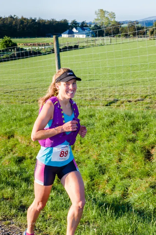 A woman is running in a field with a fence in the background.