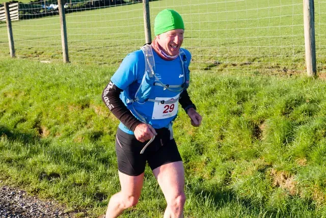 A man wearing a green hat and a blue shirt is running in a field.
