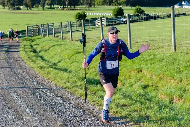 A man is running down a dirt road with walking poles.