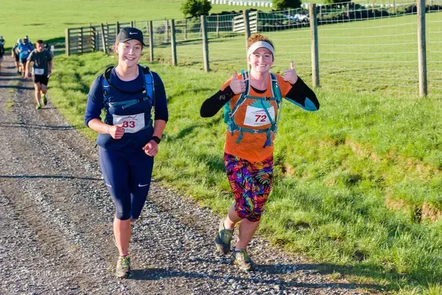 Two women are running on a dirt road in a field.