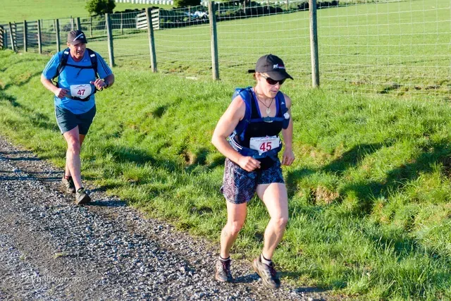 Two people are running on a dirt road in a field.