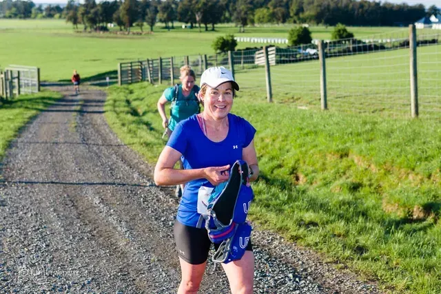 A woman is running down a dirt road in a field.