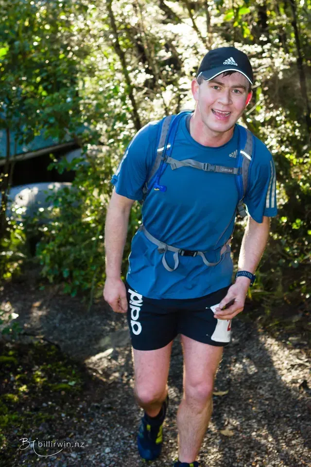A man in a blue shirt and black shorts is walking through the woods.