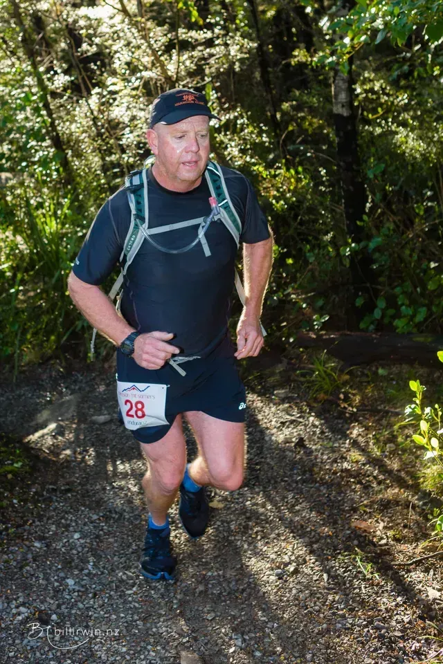 A man is running on a trail in the woods.