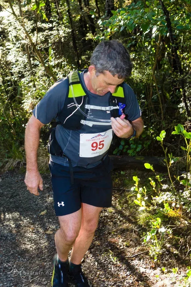 A man wearing a number 95 bib is running through the woods.