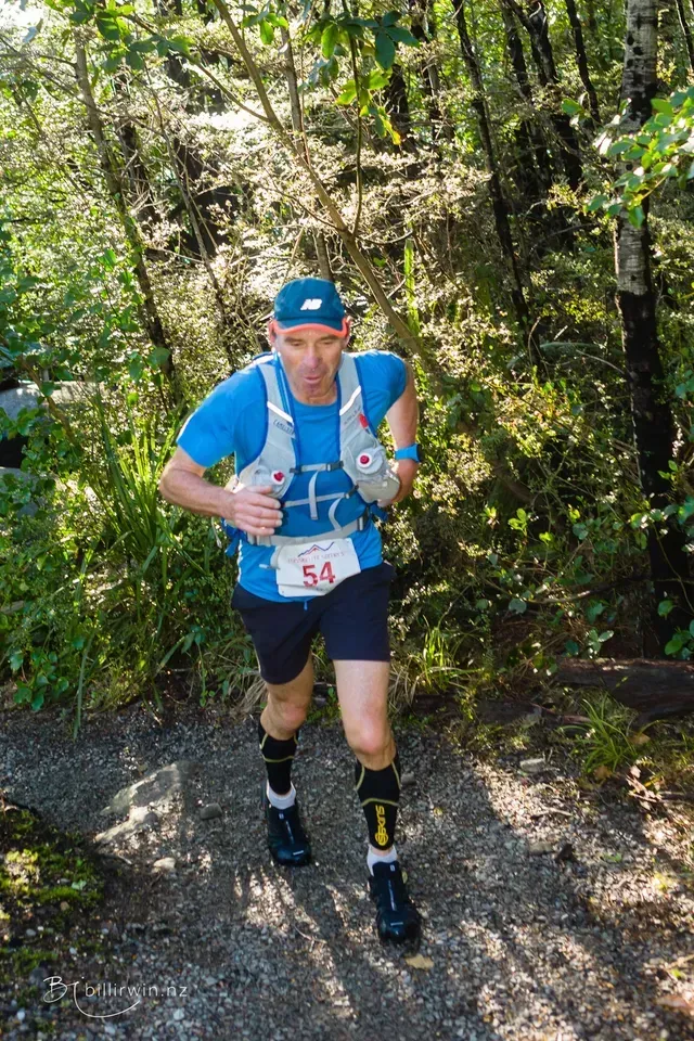 A man is running down a trail in the woods.