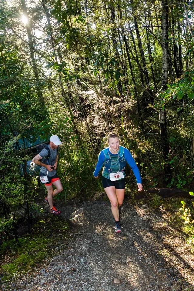 A man and a woman are walking down a trail in the woods.