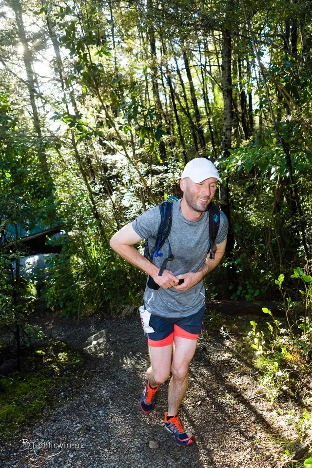 A man is running on a trail in the woods.