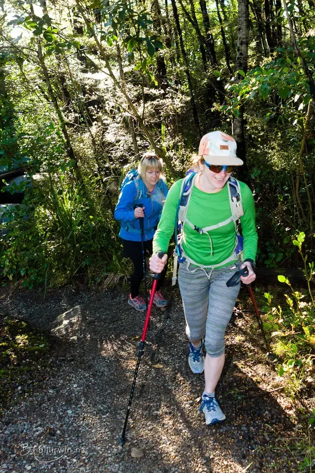 Two women are hiking down a path in the woods.