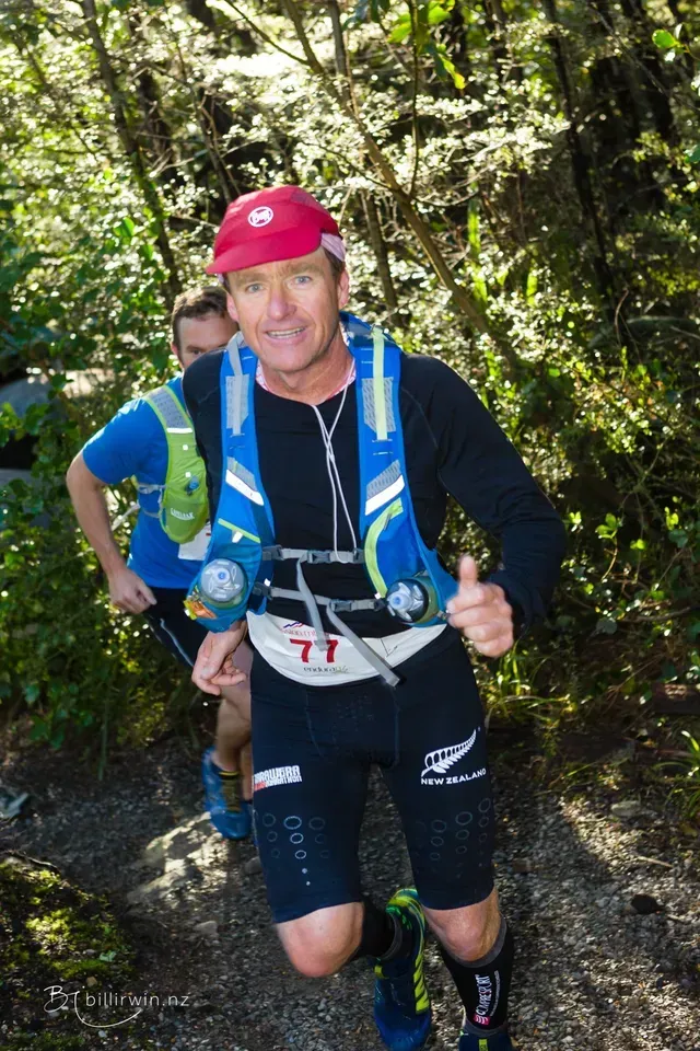 A man is giving a thumbs up while running in the woods.