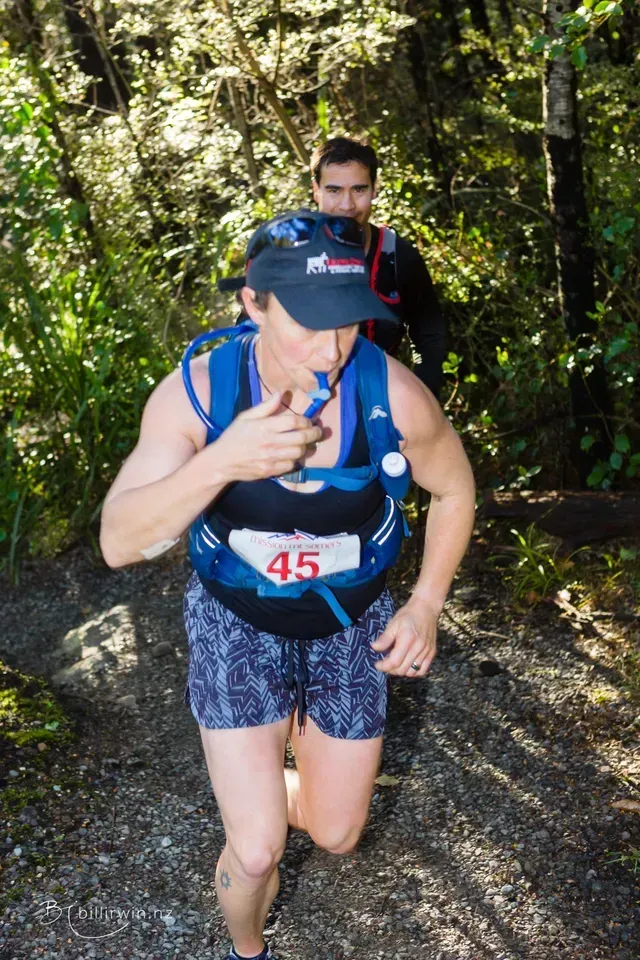 A man and a woman are running on a trail in the woods.
