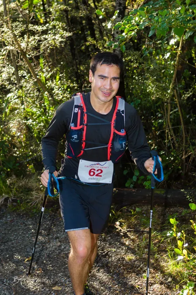 A man wearing a number 62 bib is walking through the woods.