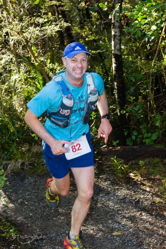 A man wearing a blue shirt with the number 82 on it is running in the woods.