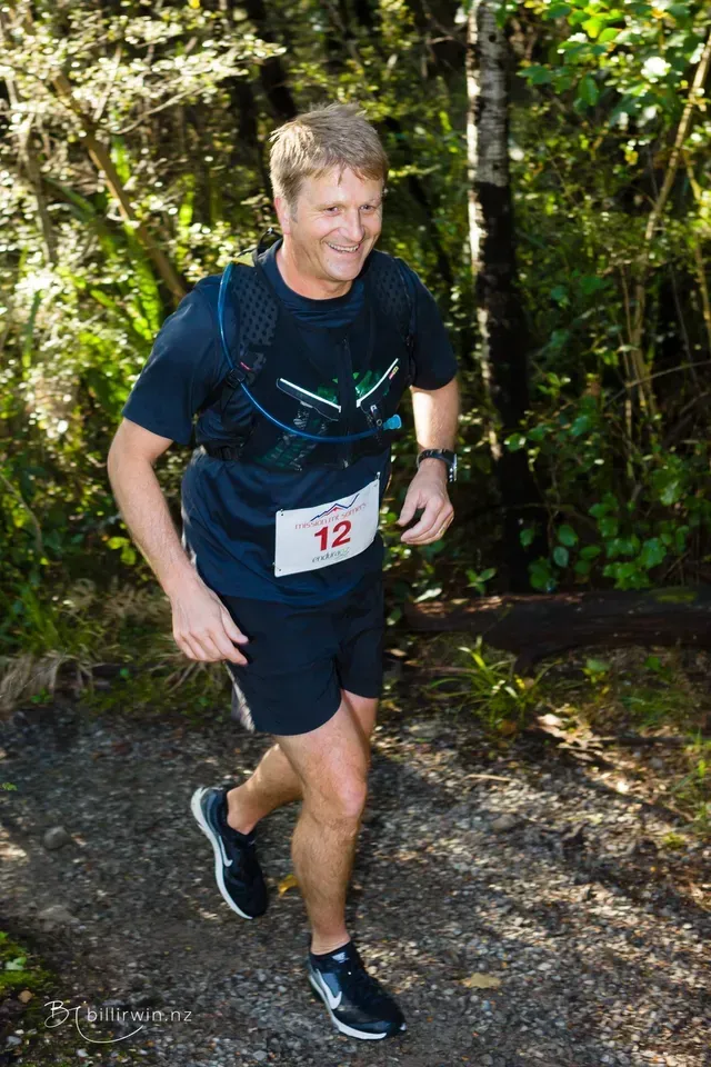 A man is running on a trail in the woods.