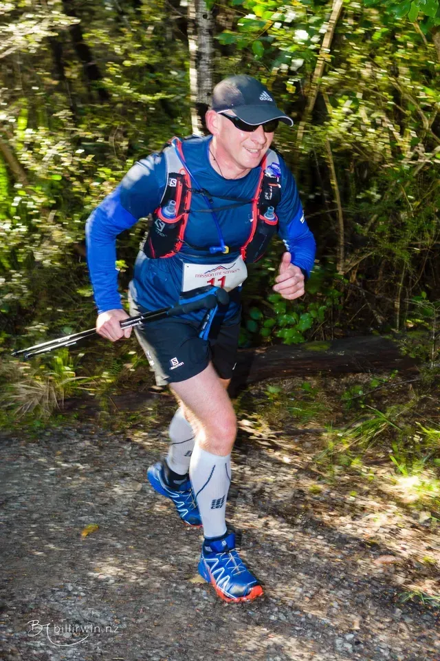 A man is running on a trail in the woods.