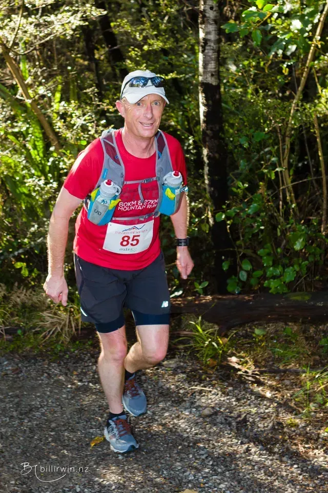 A man is running on a trail in the woods.