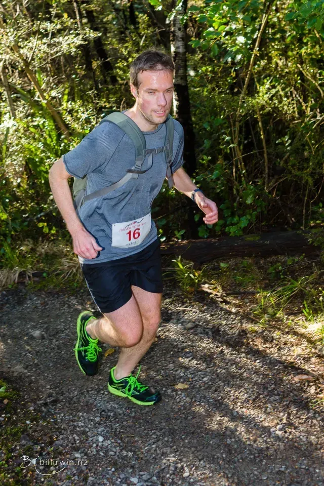 A man is running on a trail in the woods.
