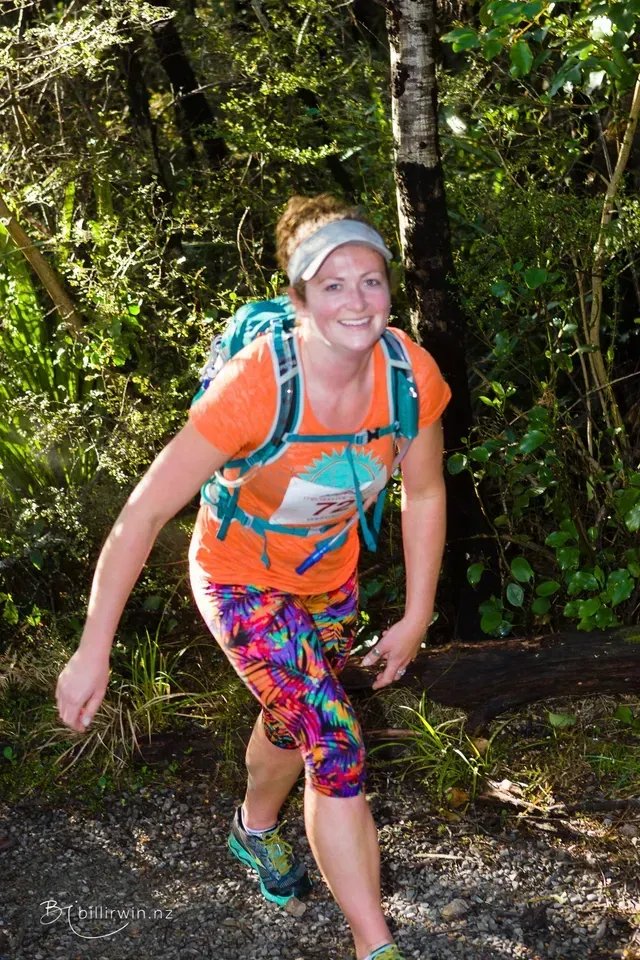 A woman with a backpack is walking through the woods.