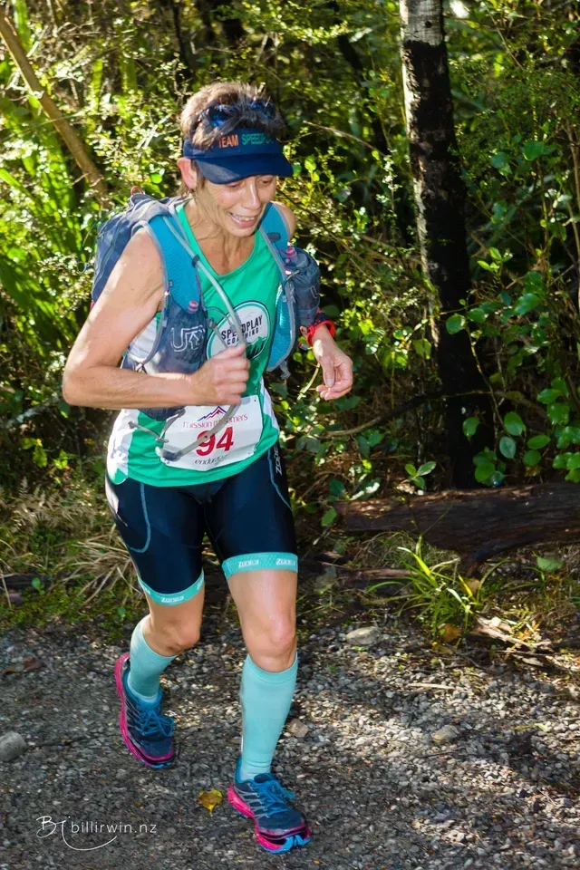 A woman is running on a trail in the woods.