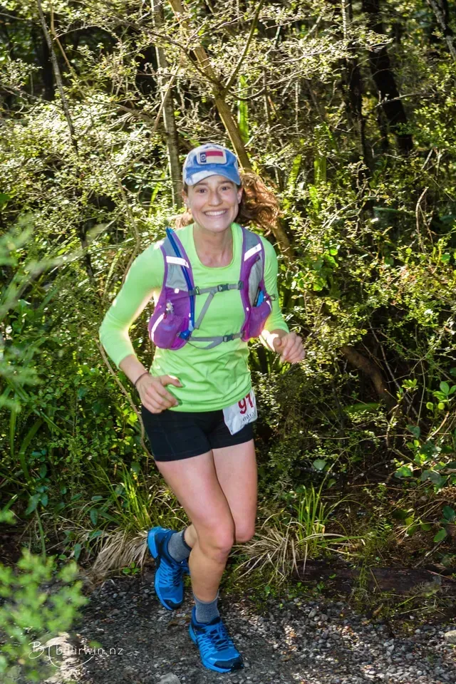 A woman is running down a trail in the woods.