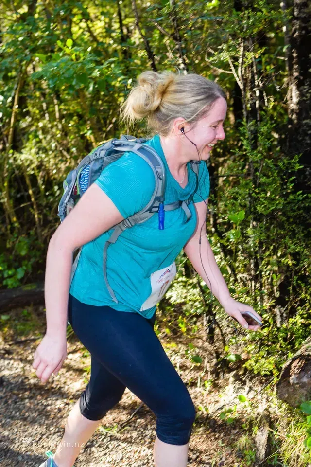 A woman with a backpack is walking down a path in the woods.