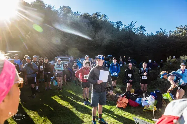 A man is giving a speech to a group of people standing in a field.