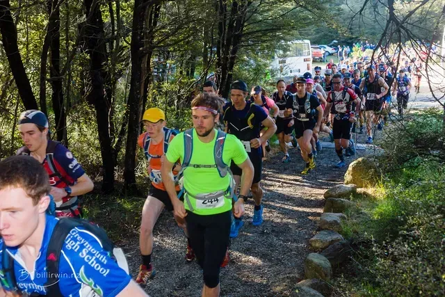 A group of people are running down a trail in the woods.