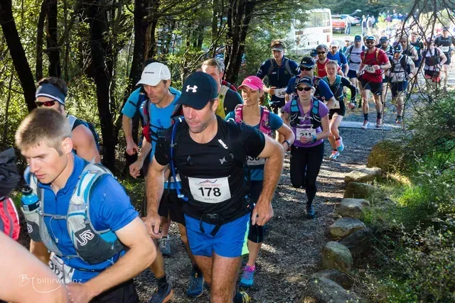 A group of people are running down a trail in the woods.